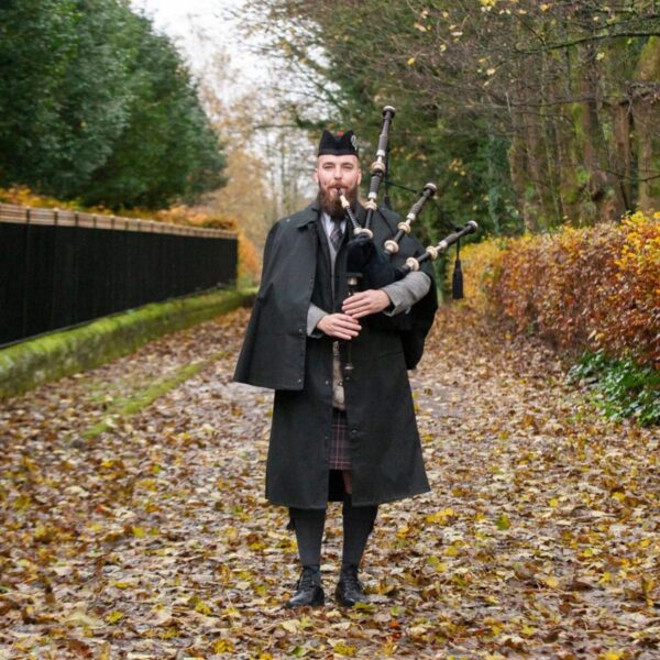 A man dressed in a kilt and Bandspec Inverness Rain Cape standing on a path with bagpipes.