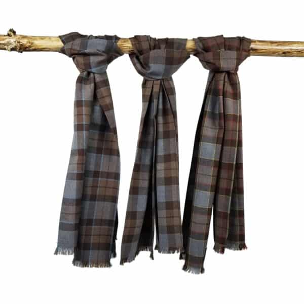 Three Tartan Scarf - OUTLANDER Premium Wool in brown, blue, and maroon tones are draped over a wooden branch, each knotted at the top.