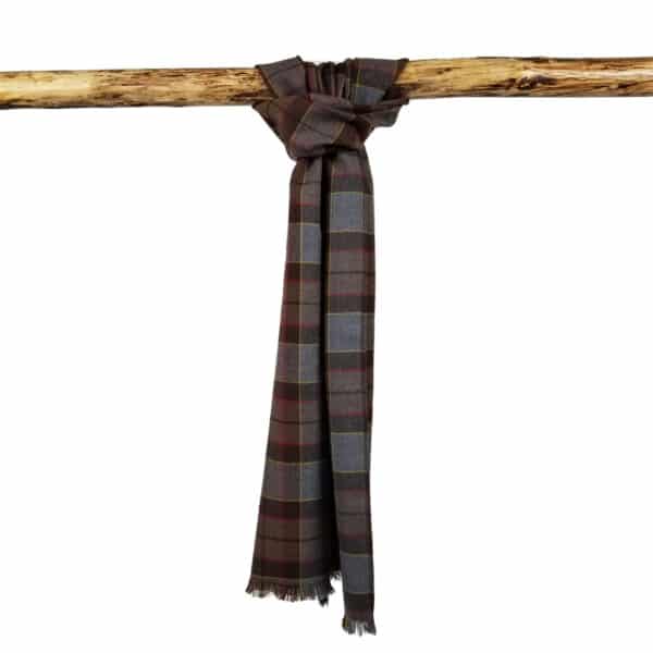 An Tartan Scarf - OUTLANDER Premium Wool in shades of brown, grey, and black hangs folded over a wooden rod against a plain white background.