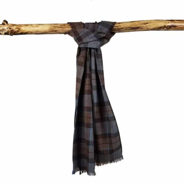 A Tartan Scarf - OUTLANDER Premium Wool, with brown and gray plaid and frayed edges, reminiscent of a weathered tartan, hangs draped over a horizontal wooden branch.