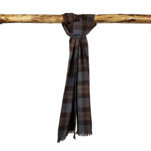 A brown and gray plaid scarf hangs folded over a horizontal wooden branch against a white background, showcasing the timeless elegance of a Tartan Scarf - OUTLANDER Premium Wool.