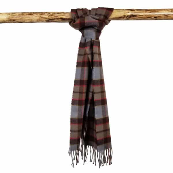 A Tartan Scarf - OUTLANDER Lambswool in shades of brown, grey, and red with fringe ends is draped over a wooden rod, reminiscent of an outlander’s rustic charm.