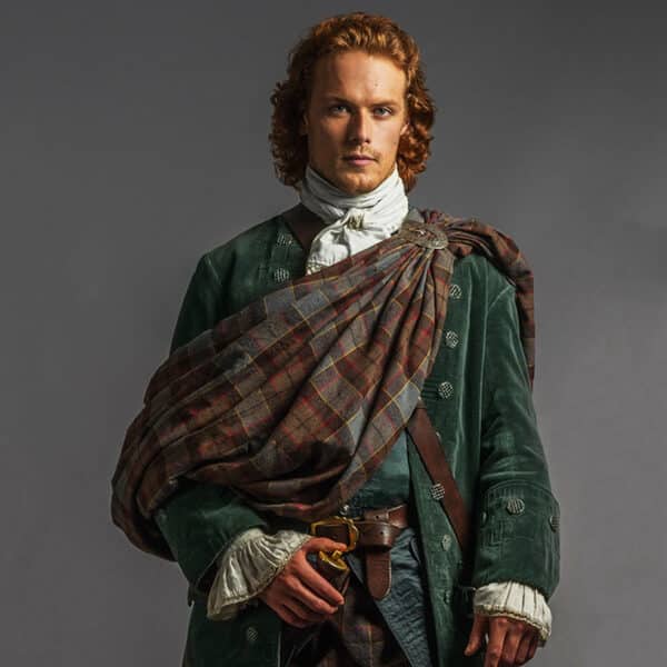 Person with long curly hair dressed in historical clothing, including a green coat and Jamie's Fraser Wedding Plaid Authentic Premium Wool Tartan sash, stands against a plain background.