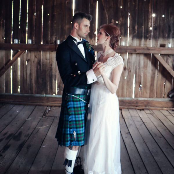 A bride and groom in kilts standing in a barn.