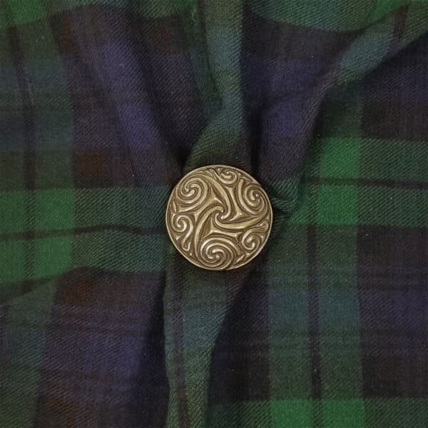 A Pictish Disc Triskelion Pin Brooch with intricate swirls is pinned to blue and green tartan-patterned fabric.