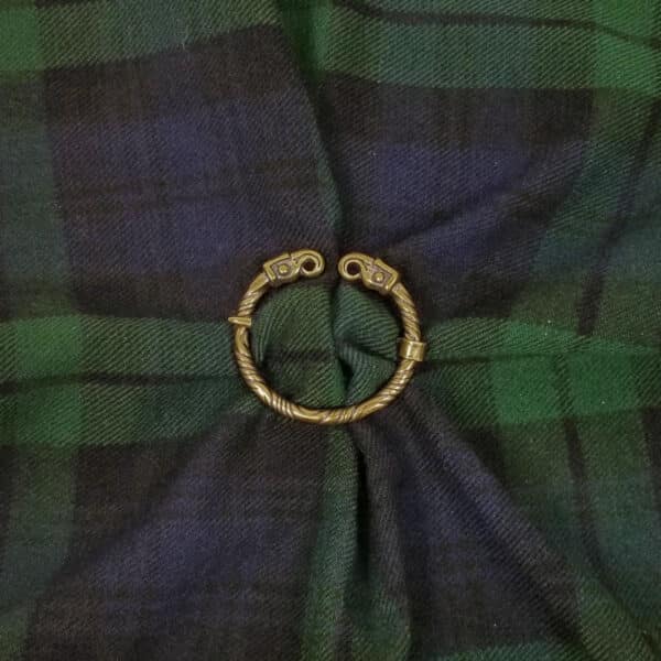 A Falcon Penannular Brooch fastens a piece of green and blue tartan fabric, reminiscent of ancient falcon motifs often seen in historical designs.