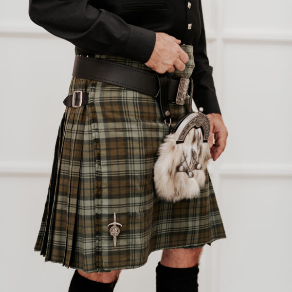 A person wearing a green tartan kilt with a sporran and a dark shirt, complemented by the Quality Pebble Grain Leather Kilt Belt, standing indoors.