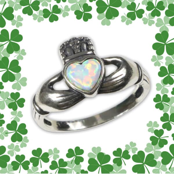 An Opal Claddagh Ring with an opal heart centerpiece, adorned with hands holding the heart and crowned, all encircled by a green cloverleaf border.