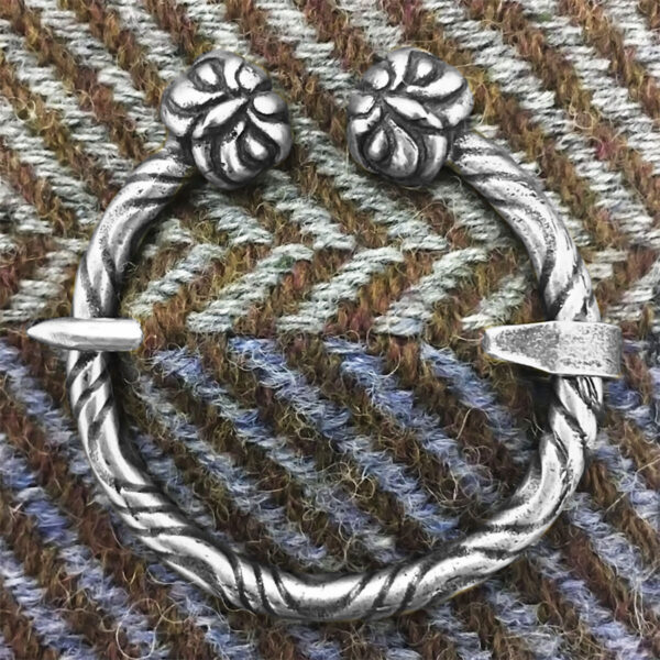 An Owl Penannular Brooch featuring a twisted rope design and two decorative ends, elegantly displayed on herringbone patterned fabric.