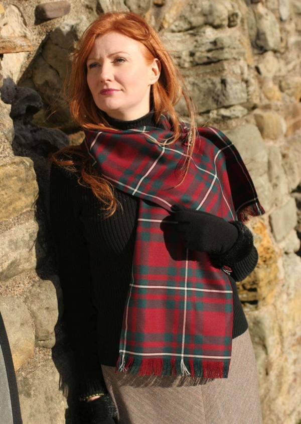 A woman with red hair is leaning against a stone wall, dressed in an Old & Rare Premium Wool Tartan Scarves Set of 2.