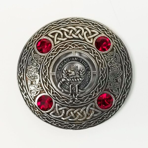 A silver belt buckle adorned with red stones and a MacLaren Clan Crest Pewter Plaid Brooch.