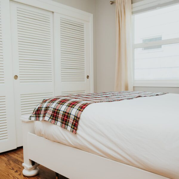 A white bed with a Stewart Dress Tartan Bed Runner - Homespun Wool Blend on it.