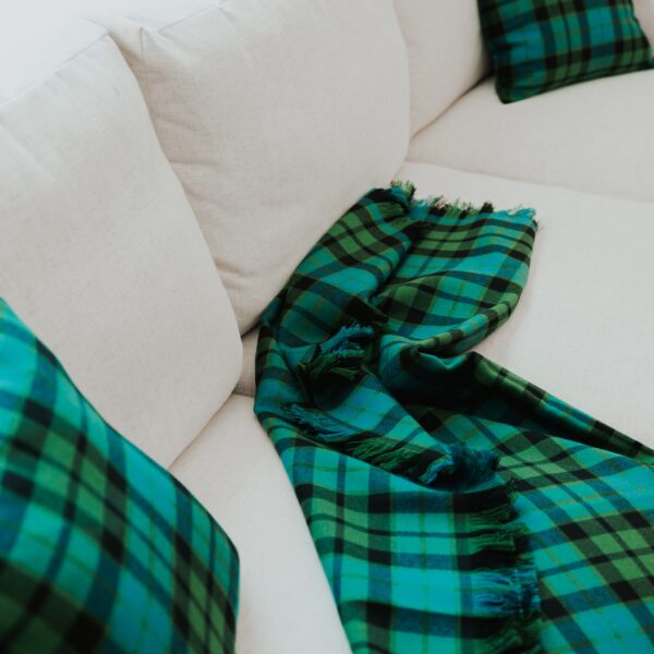 A green and black Stewart Dress Homespun Tartan blanket/throw - 2 Yards on a white couch.