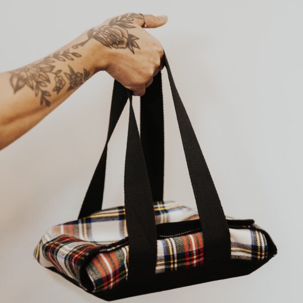 A person holding a Prince of Wales Small Tartan Casserole Carrier - Poly/Viscose Wool Free.