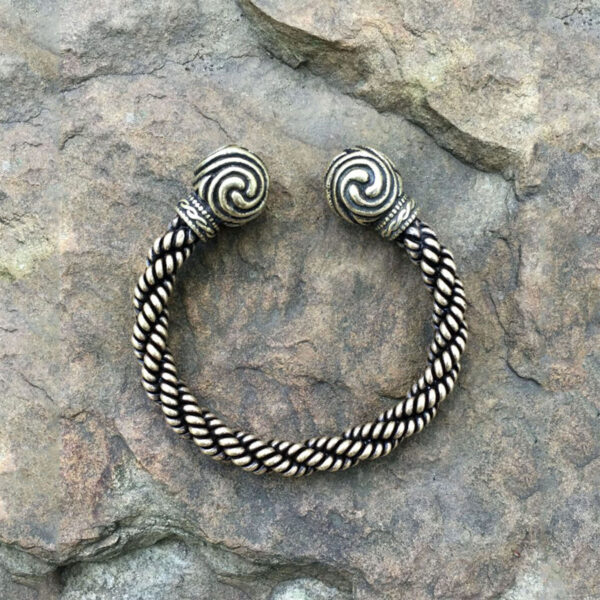 A Celtic Triskelion Bronze Torc Bracelet - 6.5in with a braided pattern on top of a rock.