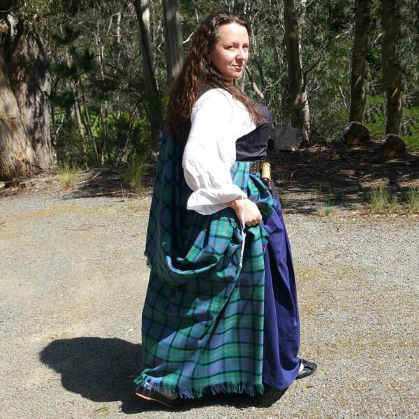 A woman dressed in a Welsh Tartan Earasaid - 13oz Medium Weight Premium Wool kilt is standing in a wooded area.