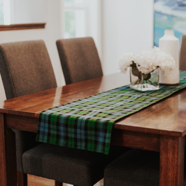 A Black Watch Ancient/Solid Green Reversible Tartan Table Runner - Homespun Wool Blend in green and blue hues graces a sturdy wooden table.