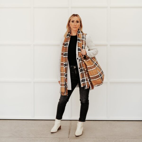 A woman is standing in front of a white wall with a Thompson Camel Modern Tartan Travel Bag - Poly/Viscose Wool Free.