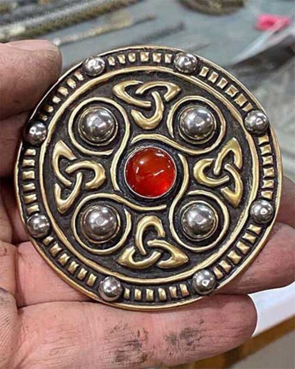 A person is holding a Jeweled Saxon Disc Brooch with a red stone.
