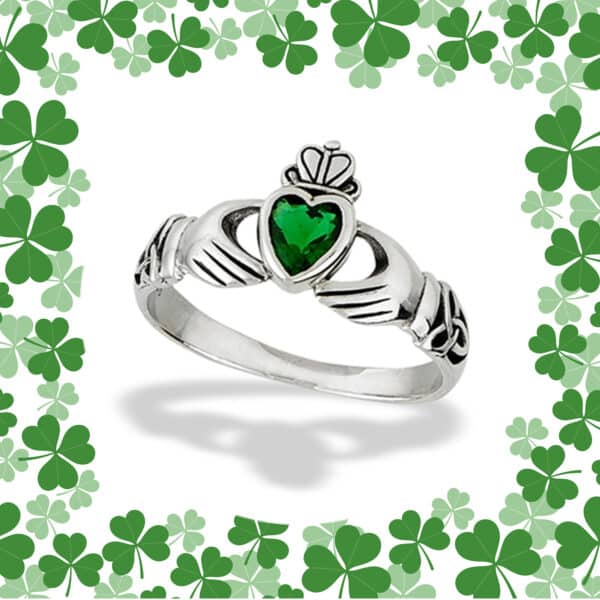 The Emerald Green Claddagh and Triquetra Ring features a silver band adorned with an emerald green heart centerpiece, encircled by an intricate border of Triquetra designs and green clovers.