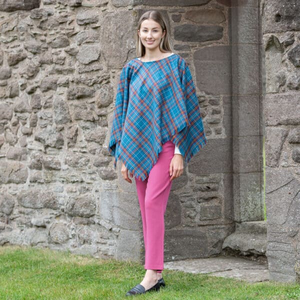 A young woman stylishly donning the Light Weight 11oz Premium Wool Tartan poncho paired with pink pants.