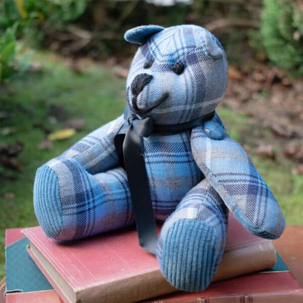 A teddy bear sitting on a stack of books covered with a Light Weight 11oz Premium Wool Tartan Bear.