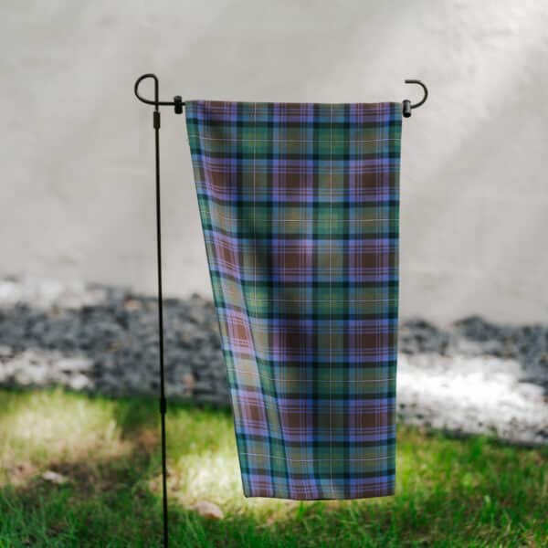 Description: An Isle of Skye Tartan Kilted Garden Flag - Wool Free Poly/Viscose hanging on a pole in the grass with a reversible tartan pattern.