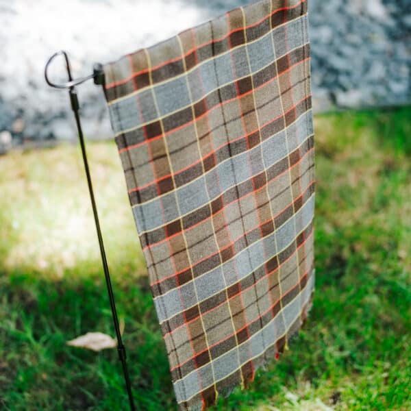 A Outlander Fraser Tartan Garden flag hanging on a pole in the grass.