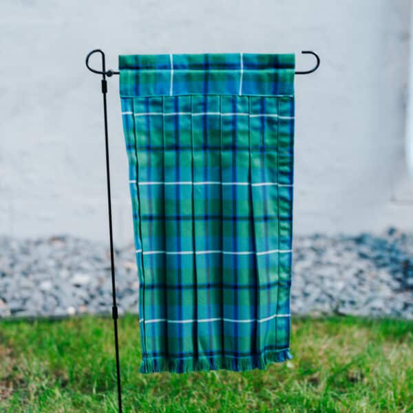A reversible Tartan Kilted Garden Flag - Wool Free Poly/Viscose, green and blue in color, hanging on a pole.
