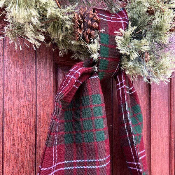 A Tartan Wreath Sash - Homespun Wool Blend hanging on a door with pine cones.