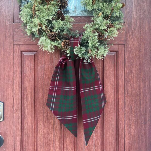 A Tartan Wreath Sash - Homespun Wool Blend hangs on a front door.