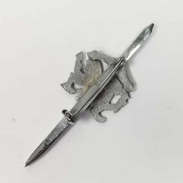 A silver-colored Welsh Dragon Kilt Pin with a segmented blade, lying on a white surface.