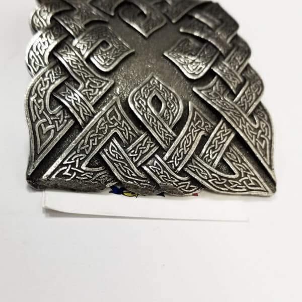The Don McKee Celtic Knot Kilt Belt Buckle features a Celtic knotwork design on a triangular shield-shaped buckle with intricate patterns, placed on a white surface.