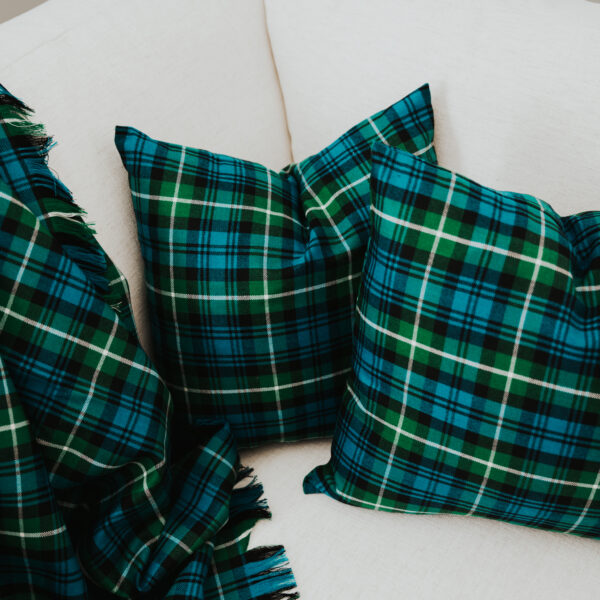 Two green and blue plaid pillows on a white couch alongside a matching plaid throw blanket.