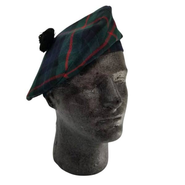 A grey mannequin head wearing a Gunn Modern Spring Weight Tartan Balmoral featuring shades of green, blue, and red with a black pom-pom on top.