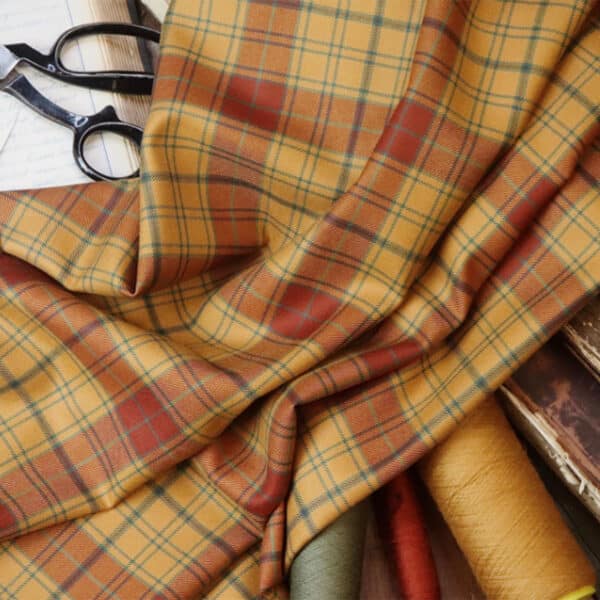 A piece of Glen Affric Tartan fabric is draped over several colored threads and books, with a pair of scissors and fabric shears placed on the side.