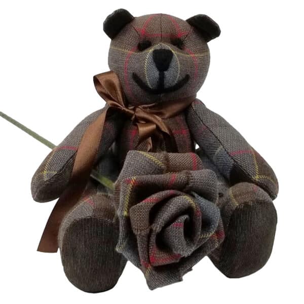 The "Outlander Tartan Heritage Bears & Roses" features a lightweight 11oz premium wool tartan bear adorned with a brown ribbon, seated upright and holding a fabric rose in its left paw.