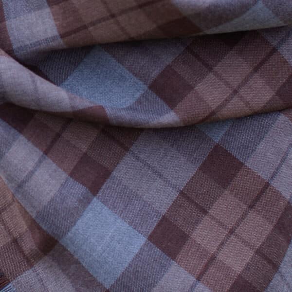 A detailed close-up of a folded fabric highlights remnants featuring the Official OUTLANDER Tartan pattern in shades of brown, gray, and blue, crafted from wool-free material, ideal for diverse projects.