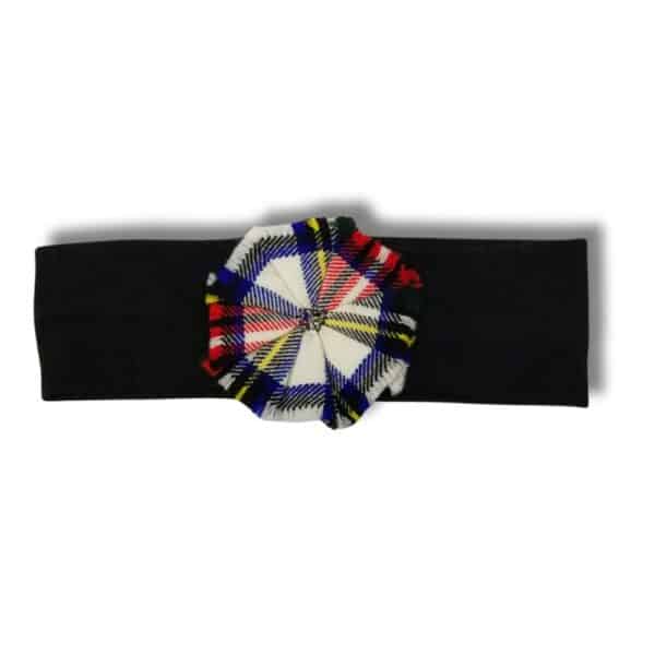 A Stewart Dress Headband in black, featuring a vibrant plaid fabric flower in red, blue, yellow, and white at its center.