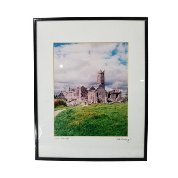 Framed photograph titled "Quinn Ireland" by Pat Conley, featuring a historic stone abbey with a tower set against a cloudy sky, surrounded by grass.