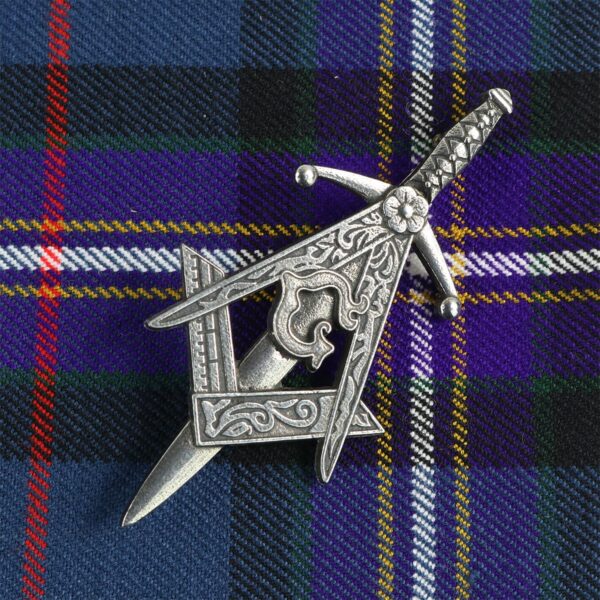 A silver Masonic Kilt Pin on a tartan with a kilt pin.