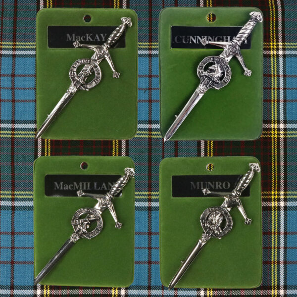 Four metal swords on a green tartan adorned with an Art Pewter Clan Crest Kilt Pin-Discontinued 6/23.