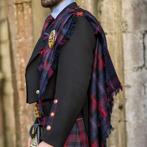 A man in a Welsh Tartan Medium Weight Premium Wool Fly Plaid kilt is standing in front of a stone wall.