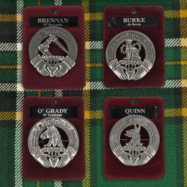 Four silver Irish Family Crest Cap Badges/Brooches on a tartan cloth.