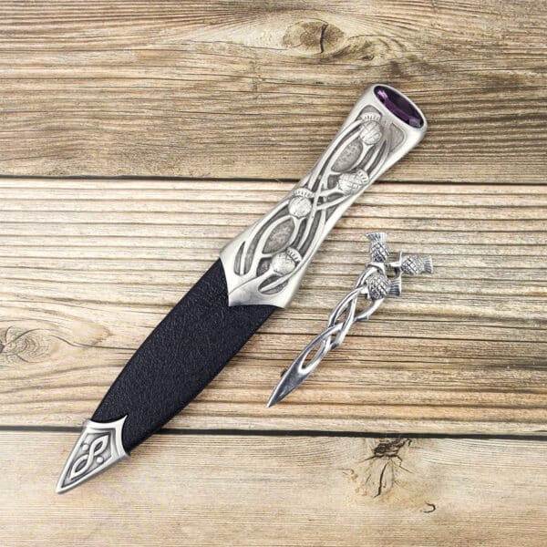 A knife with a Celtic design on it, specifically a Pewter Scottish Thistle Knot Sgian Dubh, is sitting on a wooden table.