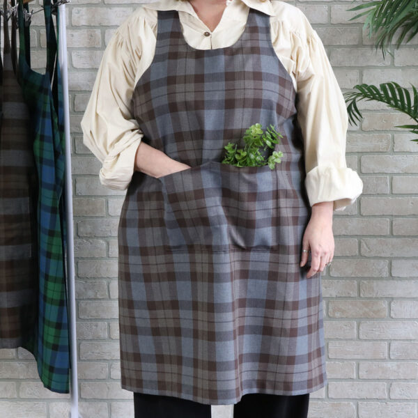 A woman wearing a Tartan Cross Back Apron - Homespun Wool Blend standing in front of a rack.