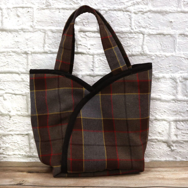 A plaid bag - Poly/Viscose Wool-Free, sitting on top of a brick wall, made from poly/viscose material and completely wool-free.