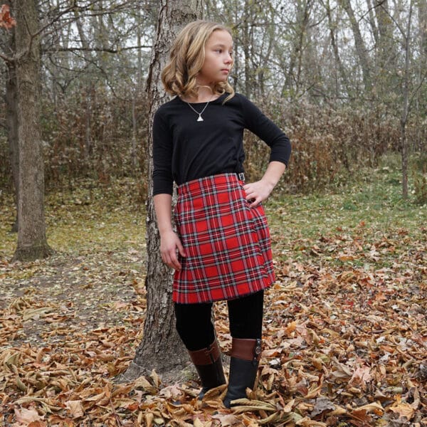 A young girl in a Premium Wool-Free Kid Kilt standing next to a tree.