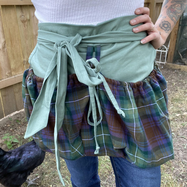 A woman wearing a plaid apron standing next to chickens.
