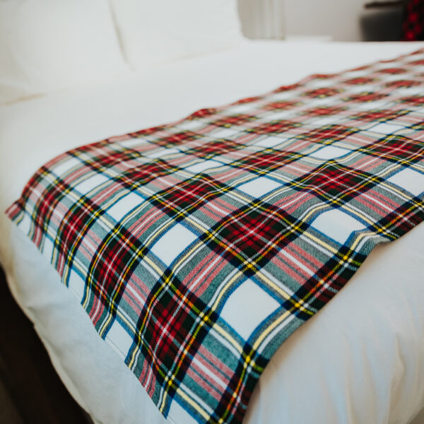 A Homespun Tartan Blanket/Throw on a bed in a hotel room.